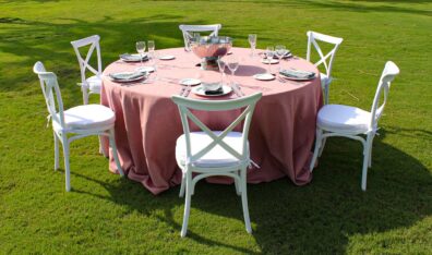 presentación de mesa redonda con mantel maquillaje carmin cristaleria, cubiertos y sillas crossback